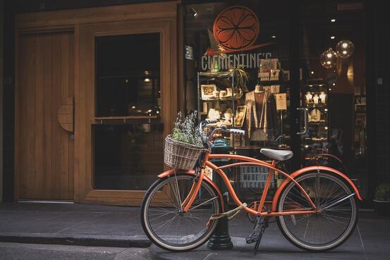 På bilde: Orange sykkel parkert ved et fortau. Bilde av  Penny from Pixabay