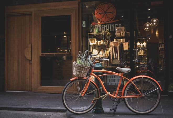På bilde: Orange sykkel parkert ved et fortau. Bilde av  Penny from Pixabay