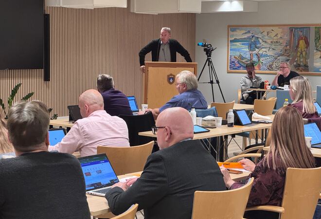 mann ved talerstol og folk som sitter i salen