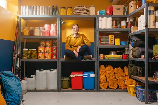 Beredskapslager hvor en mann sitter i en av hyllene. Regner med at bildet prøver å forklare at det kan være bra å ha en venn på lager.