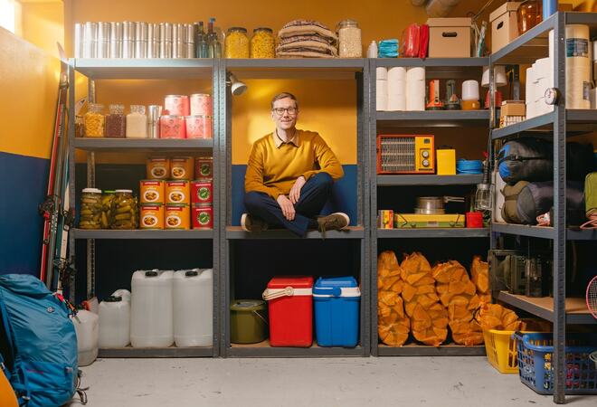 Beredskapslager hvor en mann sitter i en av hyllene. Regner med at bildet prøver å forklare at det kan være bra å ha en venn på lager.