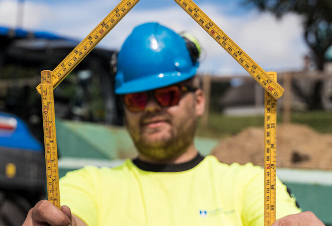 Bygningsarbeider med ein tommestokk forma som eit hus