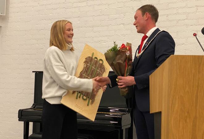 Ung kvinne frå overrekt kunstverk og blomar frå ordførar.