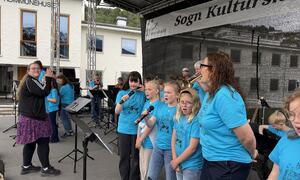 Ei gruppe born og unge som syng og spelar. Alle har blå t-skjorter med logoen til Sogn kulturskule og ei musikkmotiv.